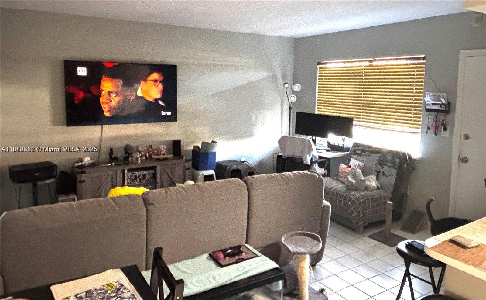 A living room features a wall-mounted television, a gray sofa, and a desk area — 7505 SW 82nd St # 318, Miami FL 33143, MIAMI, FL
