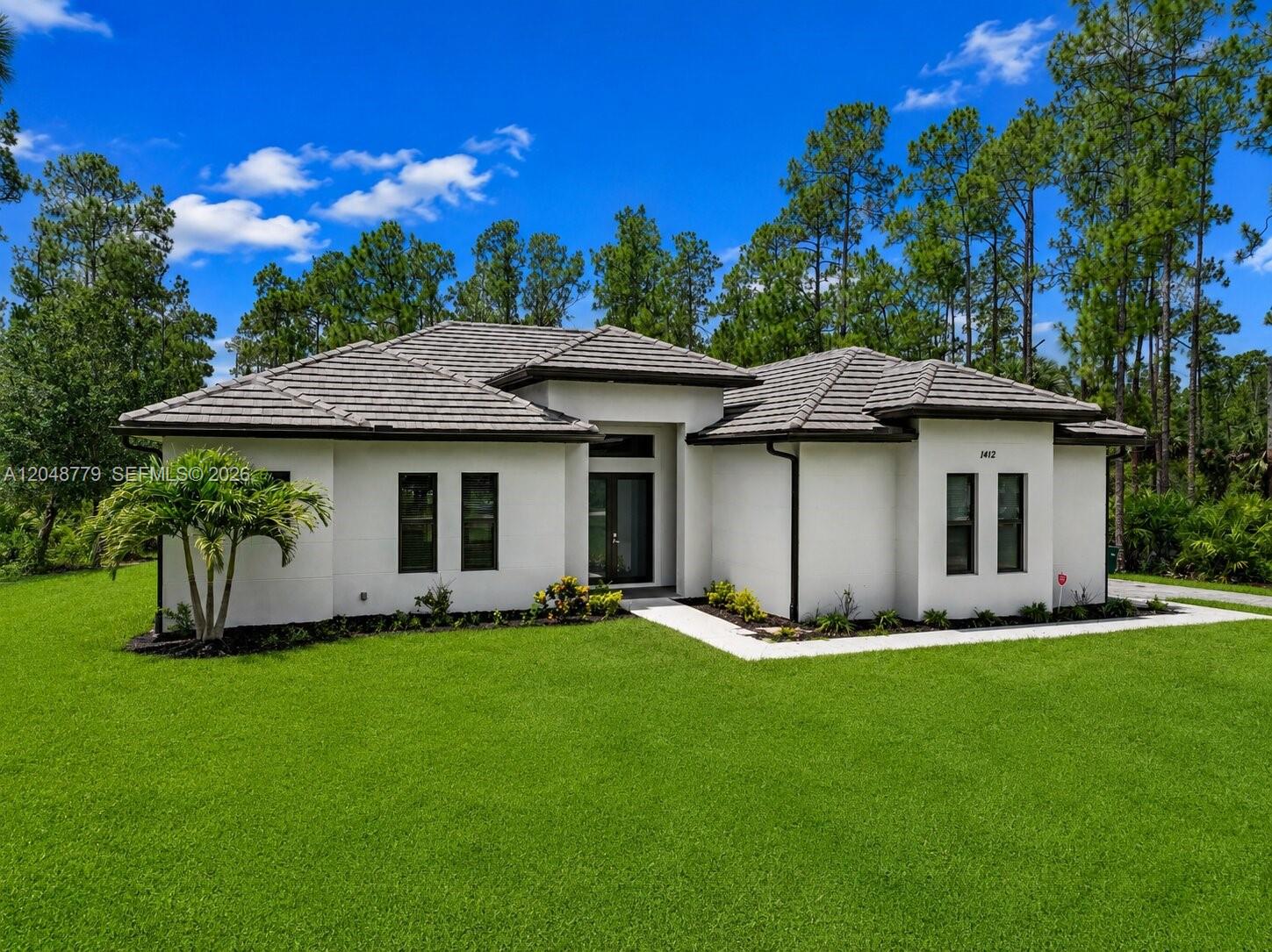 A single-story white house with a dark tiled roof sits on a green lawn — 1412 22nd Ave NE, Naples FL 34120, NAPLES, FL