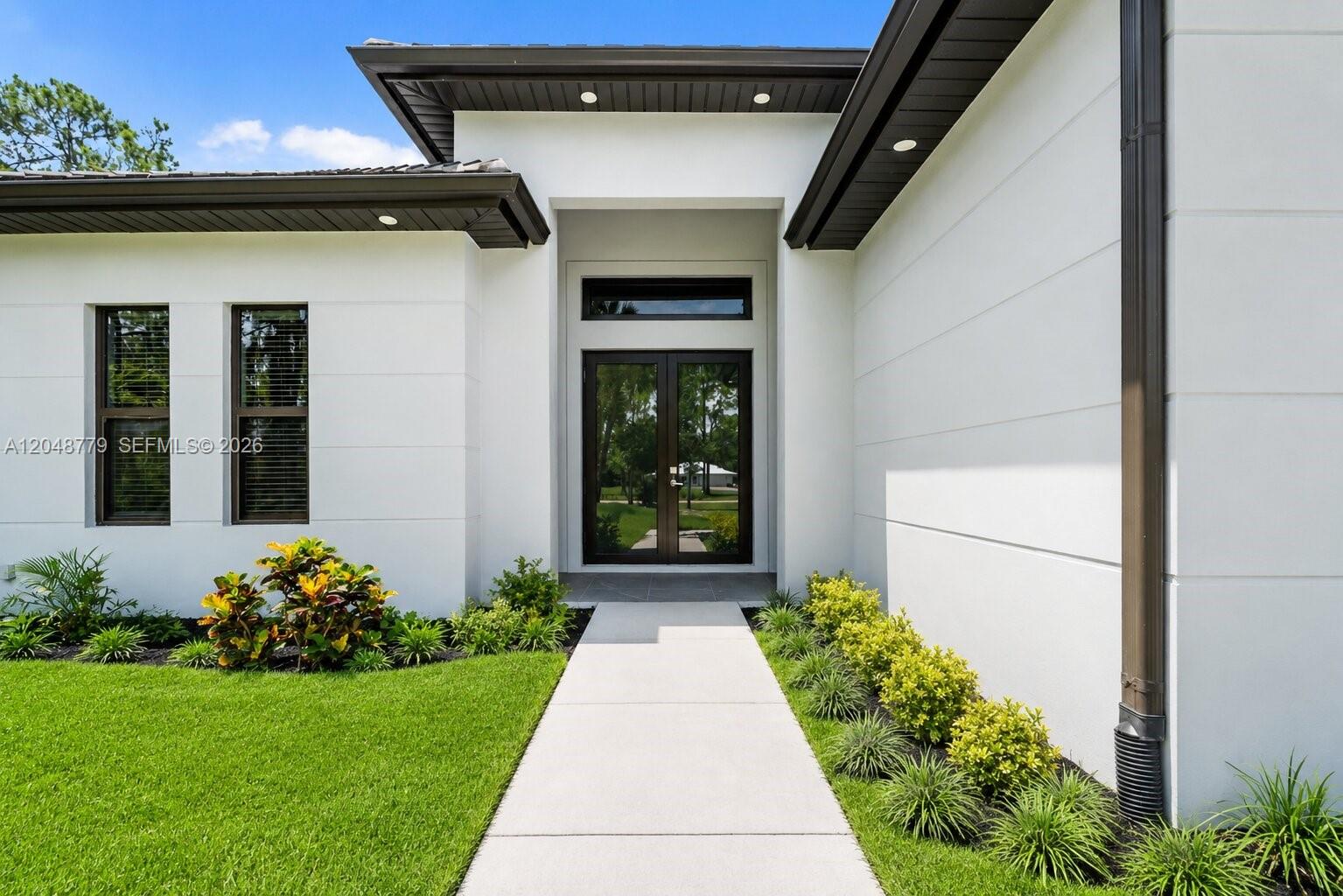 A modern white house exterior features a double front door and a concrete walkway — 1412 22nd Ave NE, Naples FL 34120, NAPLES, FL