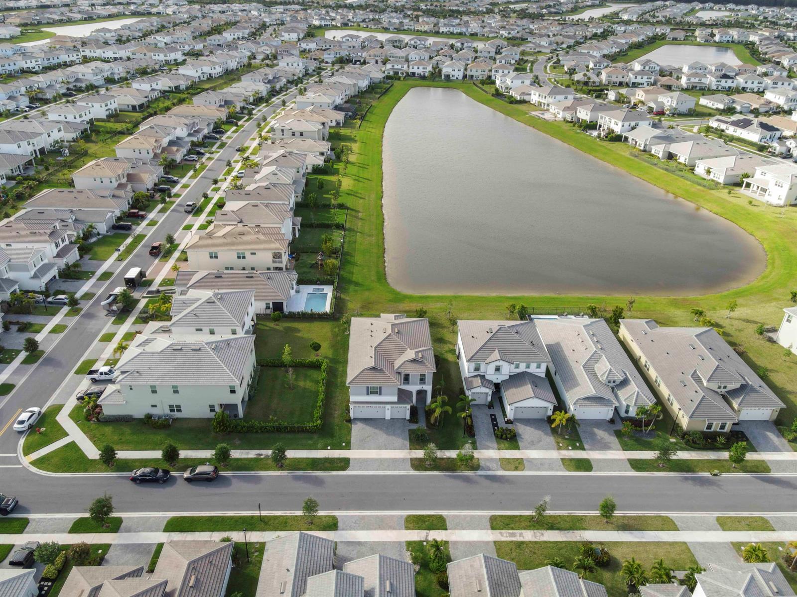 An aerial view shows a suburban neighborhood with houses surrounding a large retention pond — 5236 Liberty Lane, Westlake FL 33470, WESTLAKE, FL