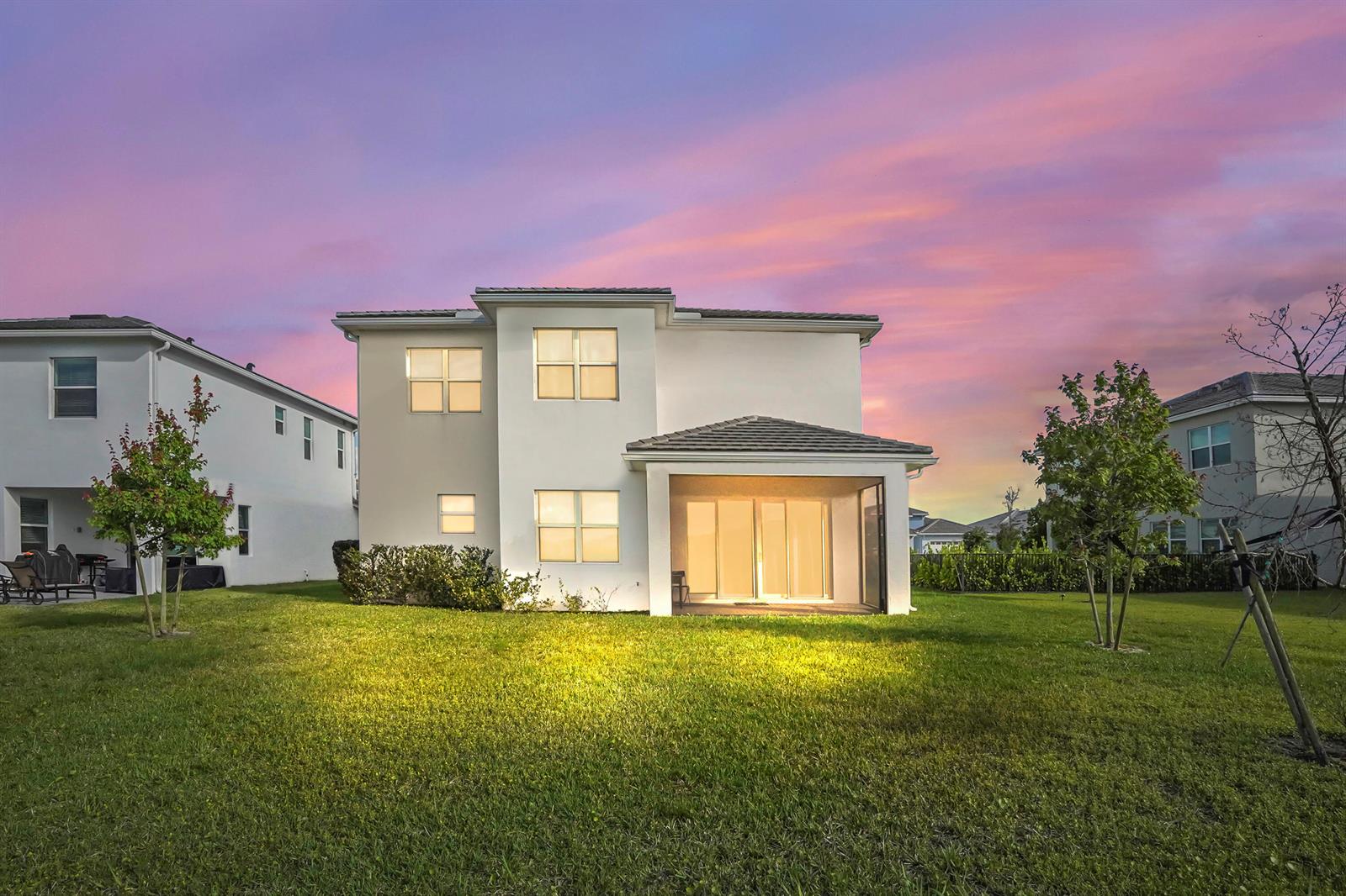 The rear exterior of a two-story white house features a covered patio and lawn — 5236 Liberty Lane, Westlake FL 33470, WESTLAKE, FL