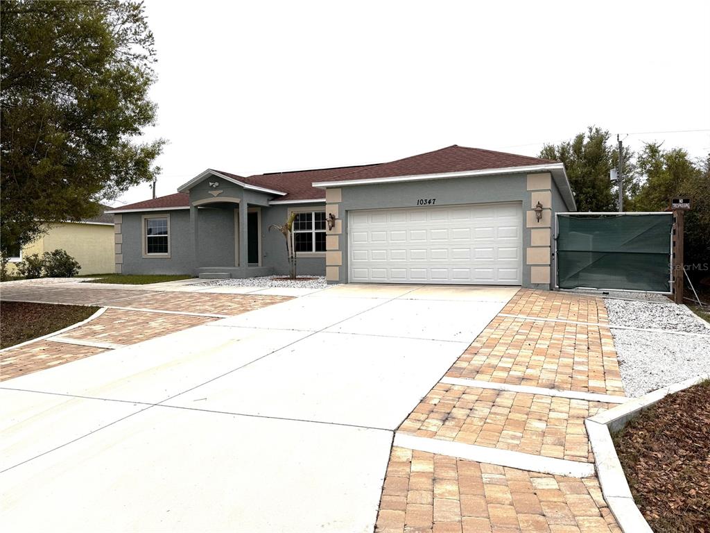 A gray single-story house features a white garage door and a paved driveway with pavers — 10347 GRAIL AVENUE, ENGLEWOOD, FL