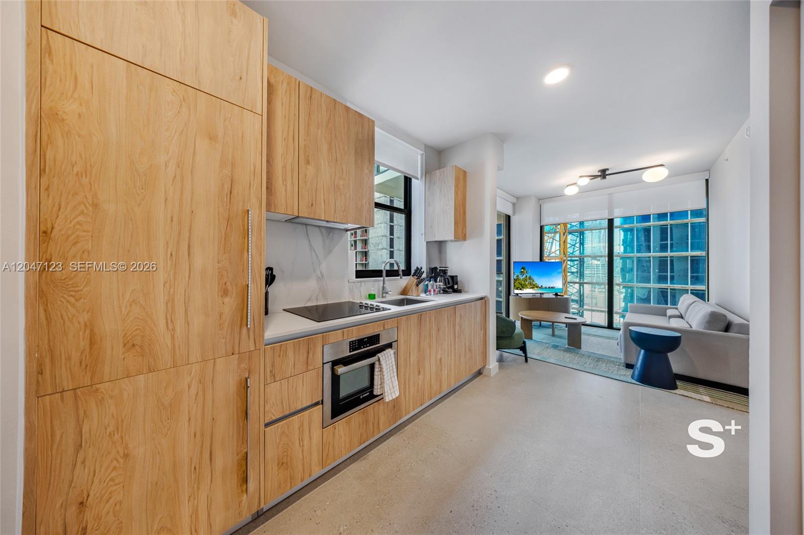 A modern kitchen with light wood cabinetry and stainless steel appliances opens into a living area — 11 NE 6th St # 2307, Miami FL 33132, MIAMI, FL