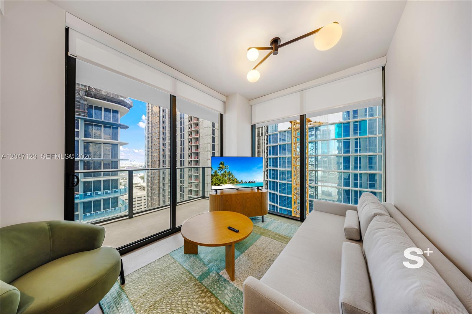 A modern living room features floor-to-ceiling windows, a light sofa, and a round wooden table — 11 NE 6th St # 2307, Miami FL 33132, MIAMI, FL