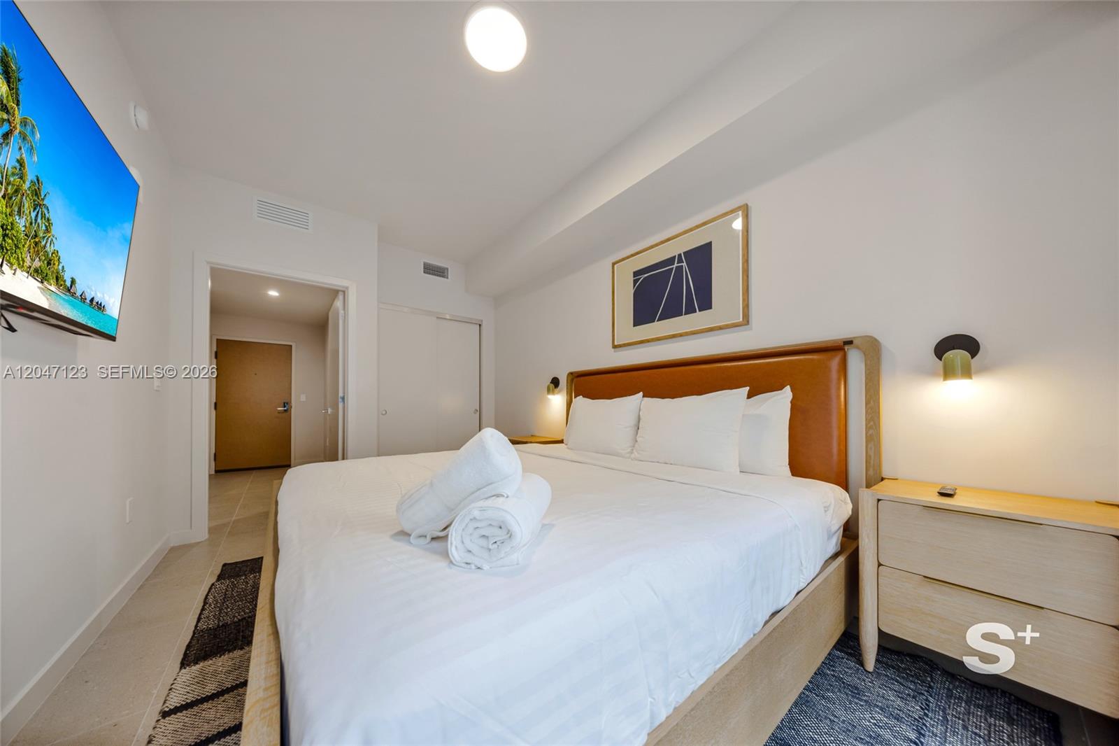 A bedroom features a king-sized bed with a leather headboard, white linens, and wall-mounted lights — 11 NE 6th St # 2307, Miami FL 33132, MIAMI, FL