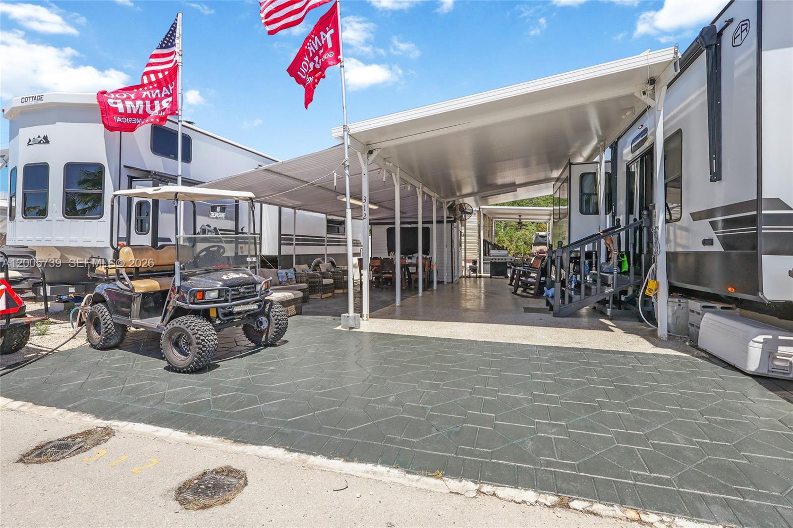 A golf cart sits on a paved patio beneath a large metal carport between two RVs — 325 Calusa St #312, Key Largo FL 33037, KEY LARGO, FL