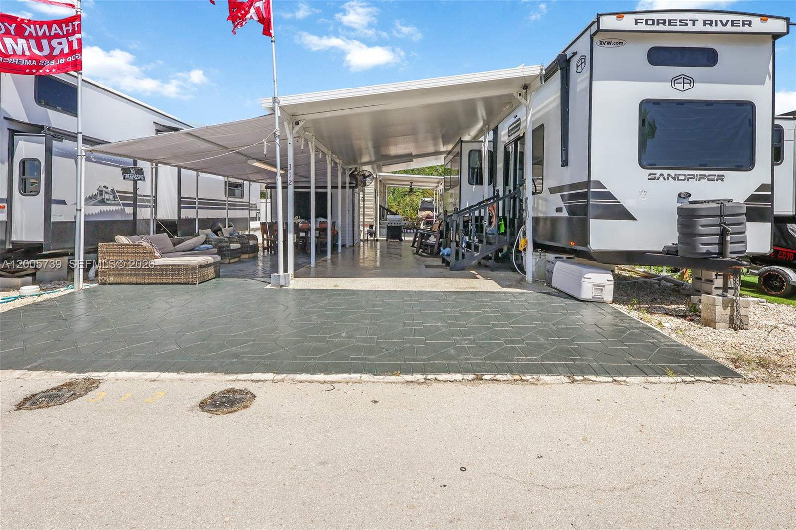 A Forest River Sandpiper RV is parked under a large metal patio cover with pavers — 325 Calusa St #312, Key Largo FL 33037, KEY LARGO, FL