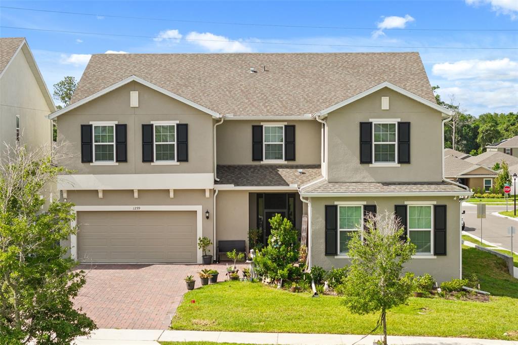 A two-story suburban house with a tan stucco exterior, dark shutters, and a two-car garage — 1299 WOODLINE DR, DELAND, FL