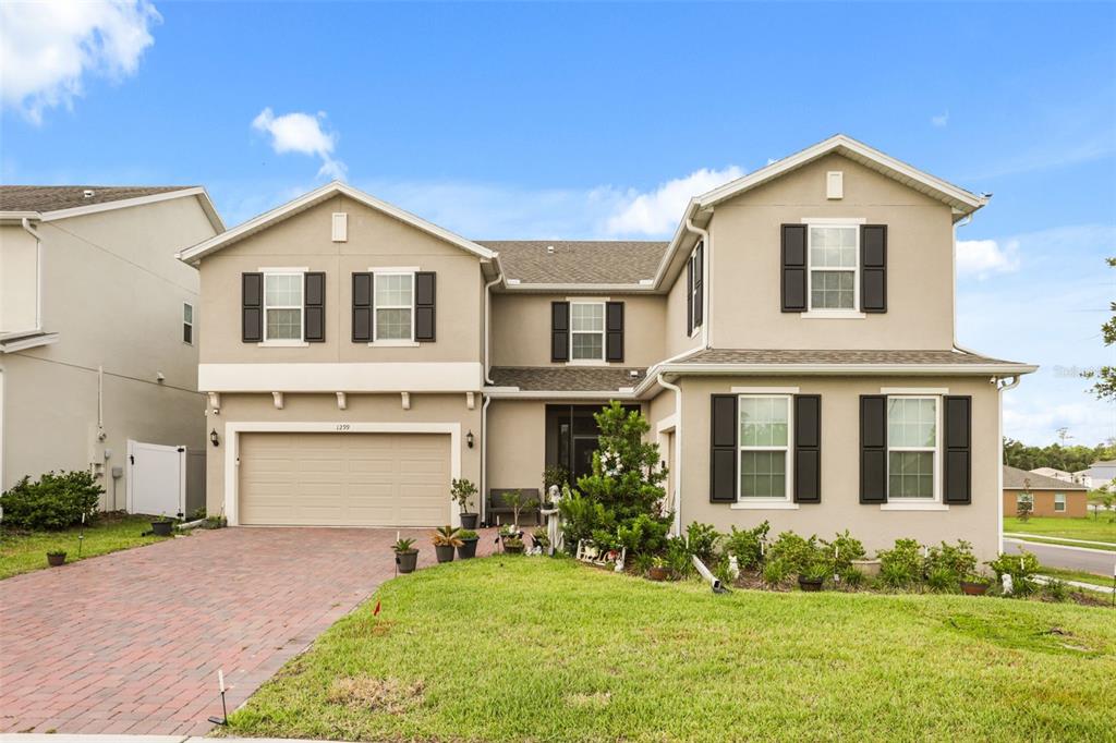 A two-story suburban house with a brick driveway, beige siding, and black window shutters — 1299 WOODLINE DR, DELAND, FL
