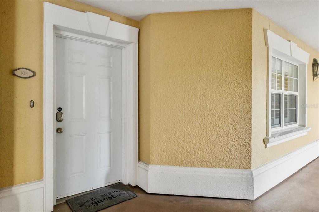 A white front door with a number 103 plaque sits on a yellow stucco wall — 7604 CABANA COURT UNIT 103, REUNION, FL
