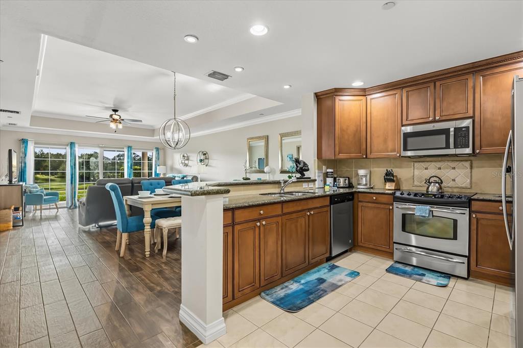 A kitchen with wood cabinets and stainless steel appliances overlooks a dining and living area — 7604 CABANA COURT UNIT 103, REUNION, FL