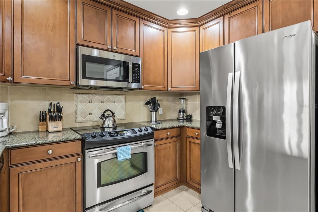 A kitchen features wood cabinets, granite countertops, and stainless steel appliances including a refrigerator and stove — 7604 CABANA COURT UNIT 103, REUNION, FL
