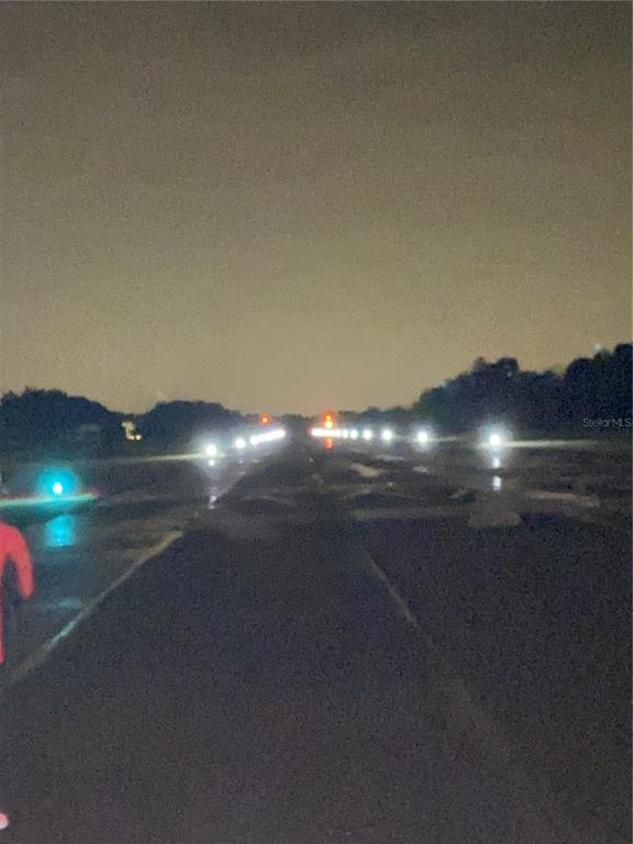 A dark, wet runway or paved path is illuminated by rows of bright white lights — 11500 PILOT COUNTRY DRIVE, SPRING HILL, FL