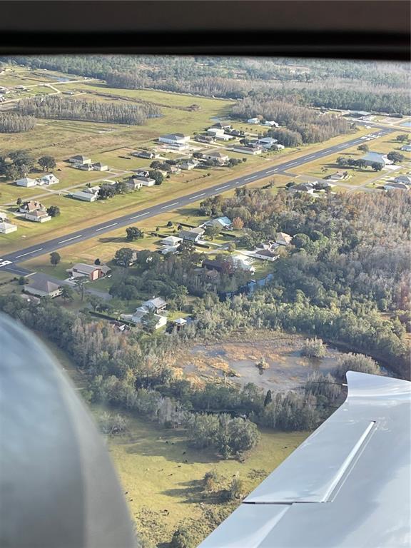 An aerial view shows a residential airpark with houses lining a paved runway and surrounding woods — 11500 PILOT COUNTRY DRIVE, SPRING HILL, FL