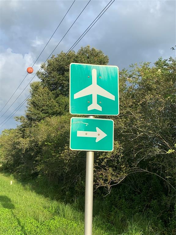 A green road sign with an airplane symbol and a right-pointing arrow on a pole — 11500 PILOT COUNTRY DRIVE, SPRING HILL, FL
