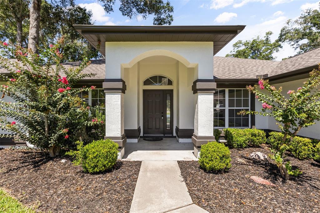 The exterior of a house features a covered entryway with a dark door and columns — 3690 SE 56TH TERRACE, OCALA, FL