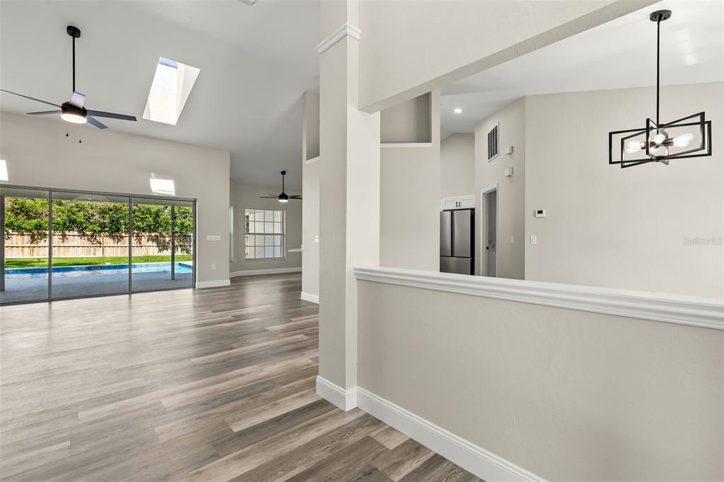 An open-concept living area features wood-look flooring, a vaulted ceiling, and a view of a pool — 3690 SE 56TH TERRACE, OCALA, FL