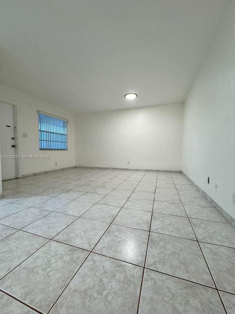 An empty room features white walls, a single window with blinds, and light-colored tiled flooring — 705 NE 2nd St # 11, Hallandale Beach FL 33009, HALLANDALE BEACH, FL