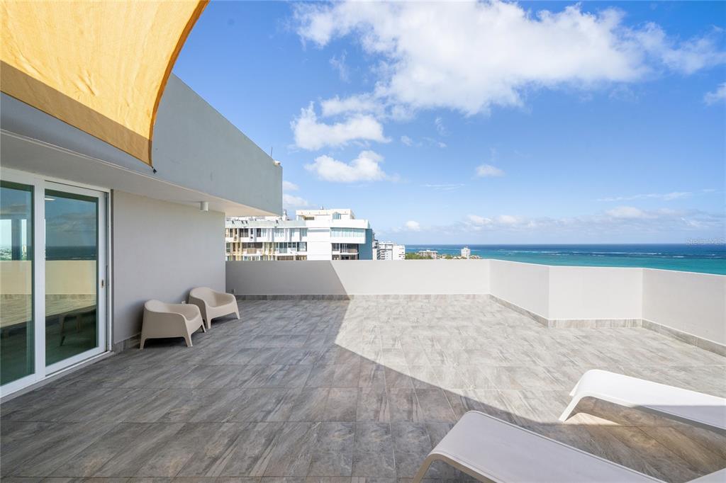 A spacious outdoor balcony features tiled flooring, lounge chairs, and a view of the ocean — 4123 ISLA VERDE AVE, WALDORF TOWER UNIT PH-4, CAROLINA, PR