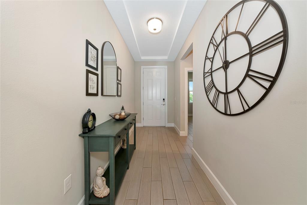 A hallway features light wood-look tile flooring, a console table, wall art, and a large clock — 13513 FLAT WOODS TERRACE, BRADENTON, FL