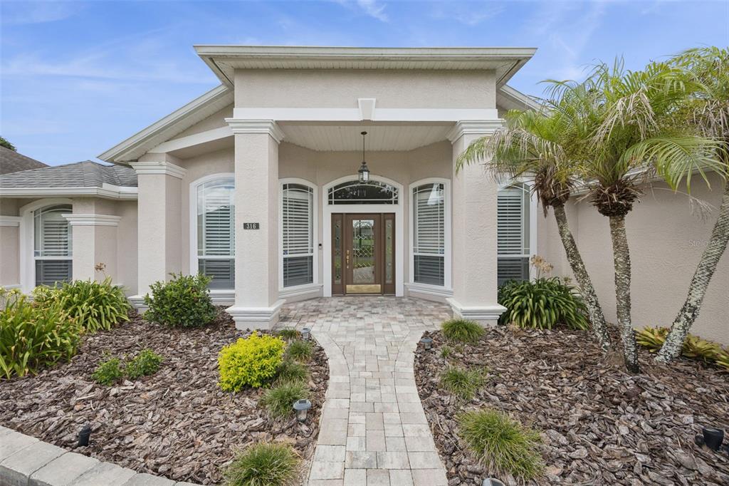 A beige house exterior features a stone walkway leading to a covered front entryway — 316 HAZELTINE DRIVE, DEBARY, FL