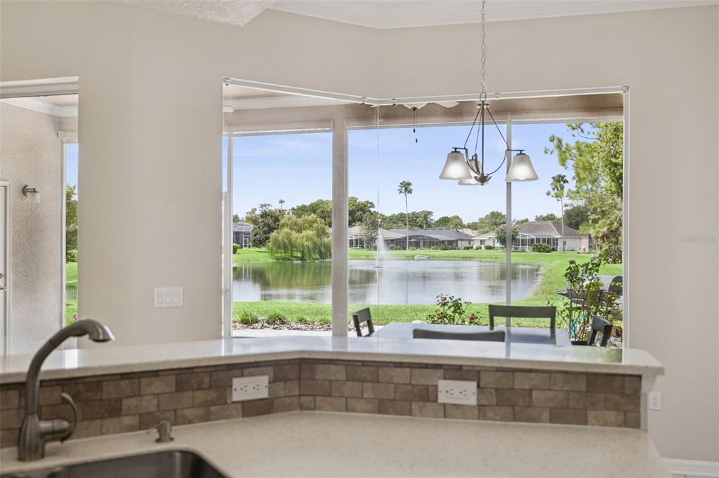 A kitchen counter with a tiled backsplash overlooks a lake through large windows — 316 HAZELTINE DRIVE, DEBARY, FL