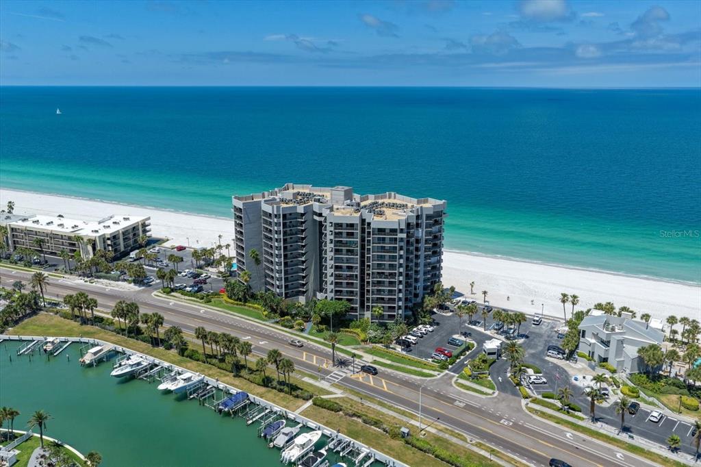 An aerial view shows a multi-story beachfront condominium building situated between a road and ocean — 1660 GULF BOULEVARD UNIT 403, CLEARWATER BEACH, FL