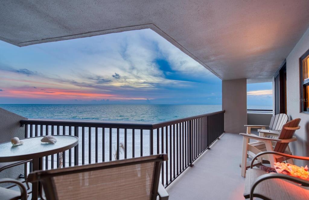 A balcony with a metal railing overlooks the ocean at sunset with outdoor seating — 1660 GULF BOULEVARD UNIT 403, CLEARWATER BEACH, FL