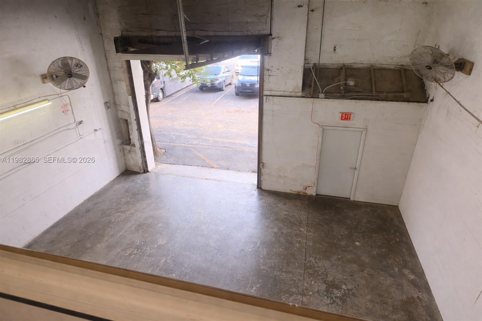 An interior view of a warehouse space with a concrete floor, roll-up door, and exit — 2016 NW 55th Ave, Margate FL 33063, MARGATE, FL