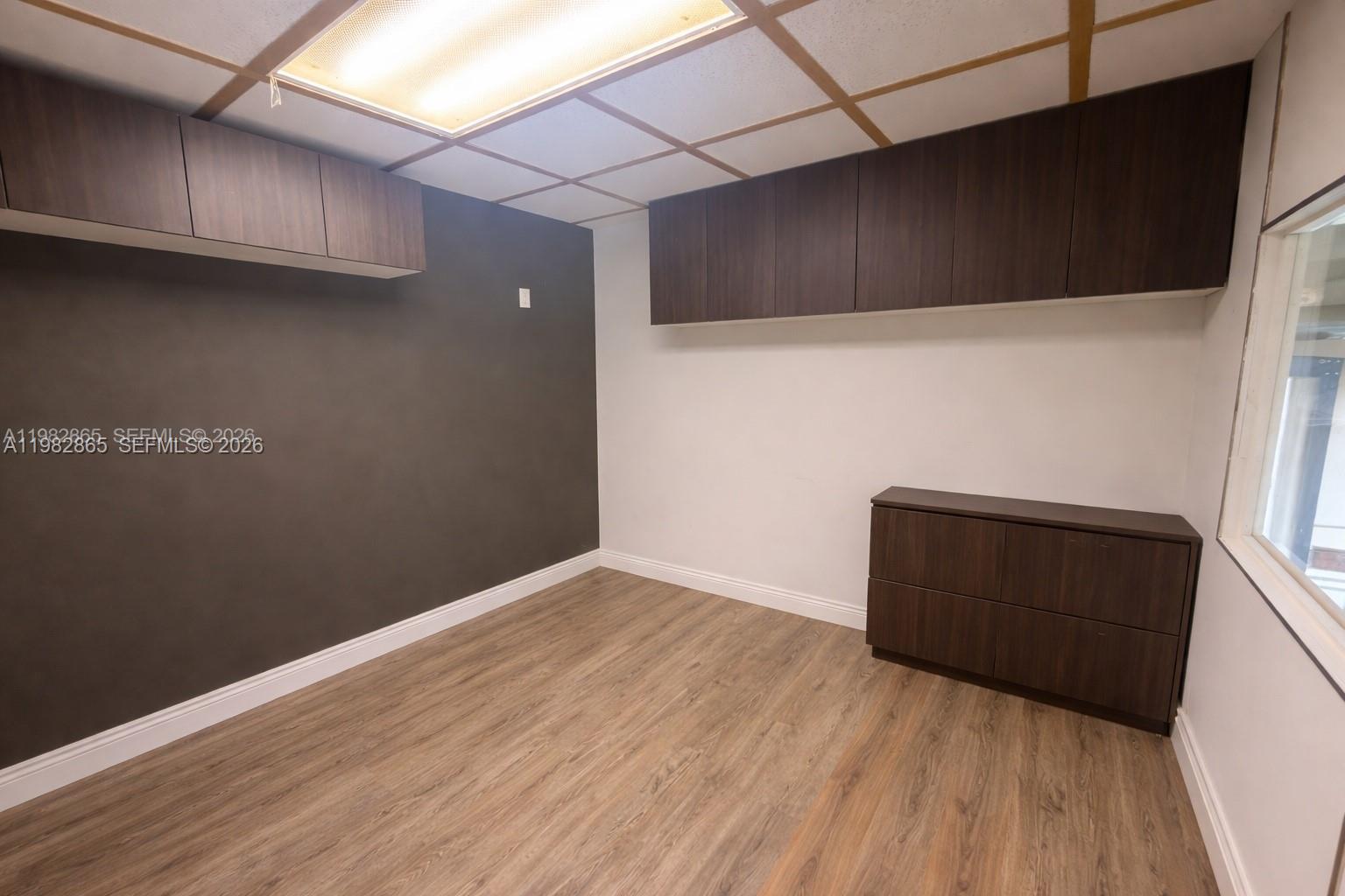 An office room features dark wood cabinetry, a grey accent wall, and wood-look flooring — 2016 NW 55th Ave, Margate FL 33063, MARGATE, FL
