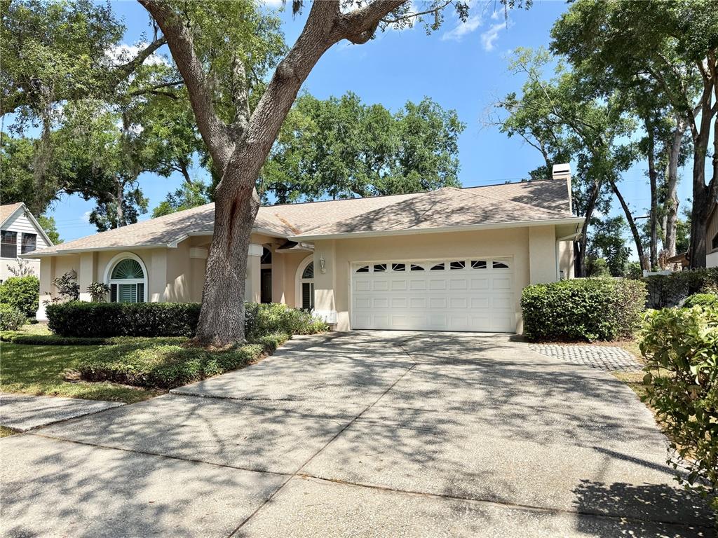 A single-story house with a beige stucco exterior, a two-car garage, and large oak trees — 6326 N QUEENSWAY DR, TEMPLE TERRACE, FL