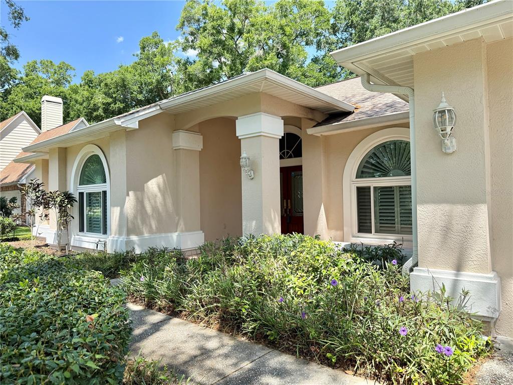 The exterior of a beige house features a covered entryway, arched windows, and landscaping — 6326 N QUEENSWAY DR, TEMPLE TERRACE, FL
