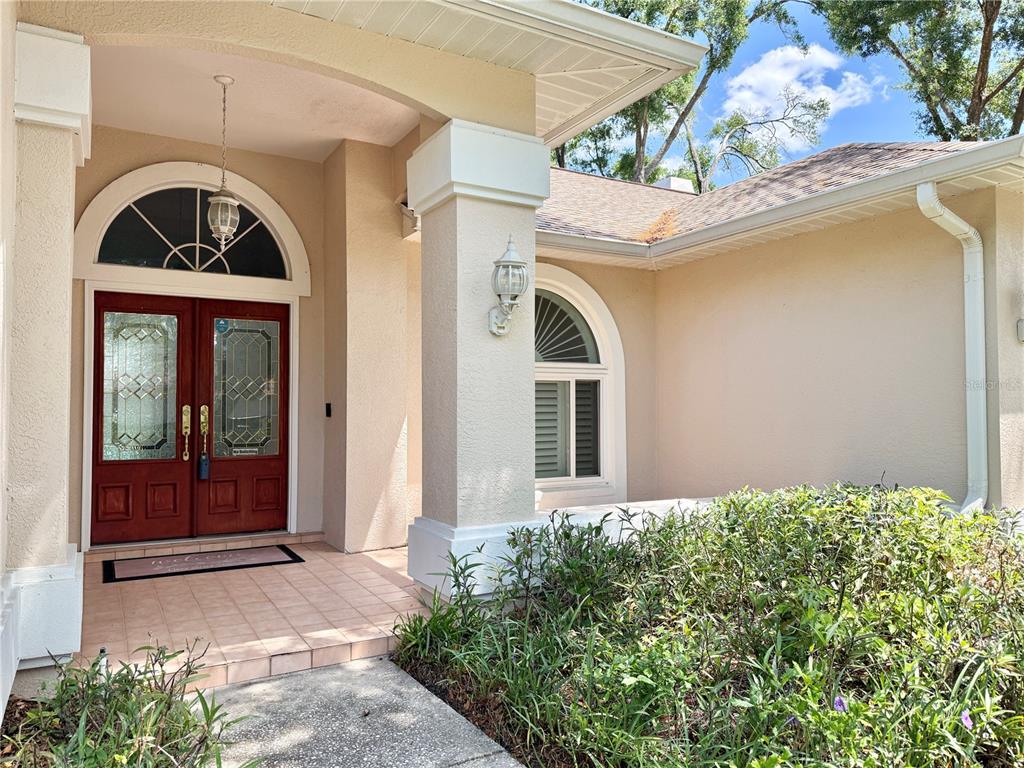 A beige house exterior features a red double front door and an arched window — 6326 N QUEENSWAY DR, TEMPLE TERRACE, FL