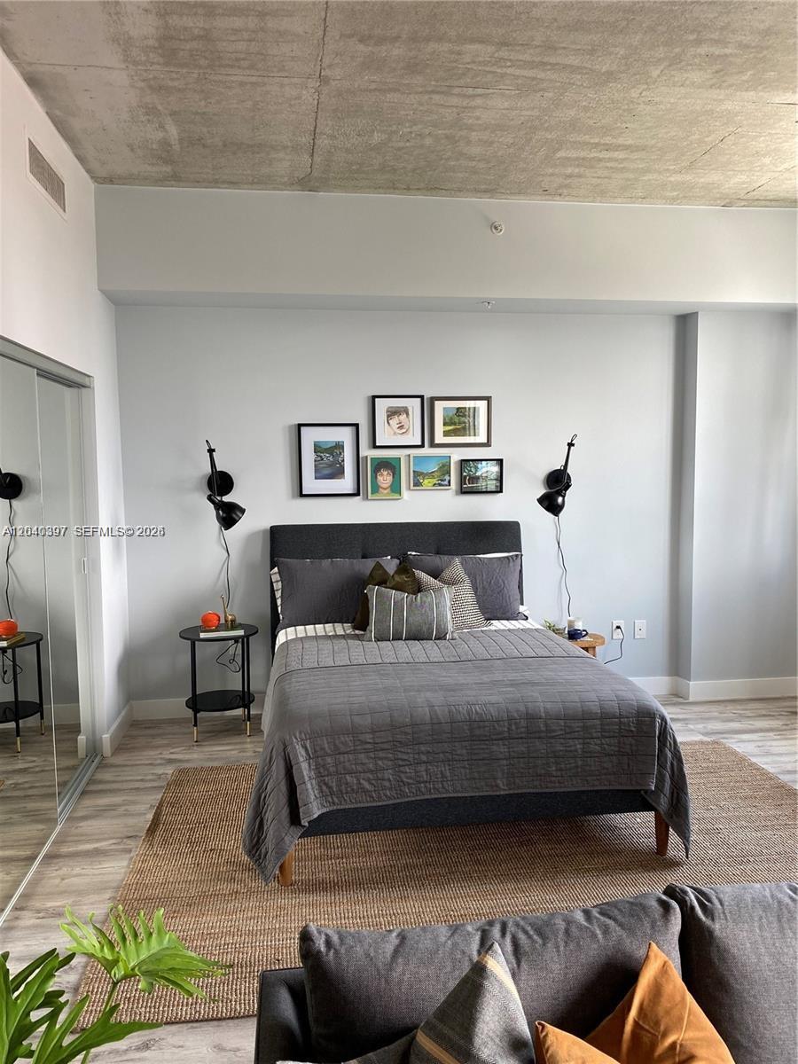 A bedroom features a gray upholstered bed, wall-mounted lamps, and a concrete ceiling — 133 NE 2nd Ave # 915, Miami FL 33132, MIAMI, FL