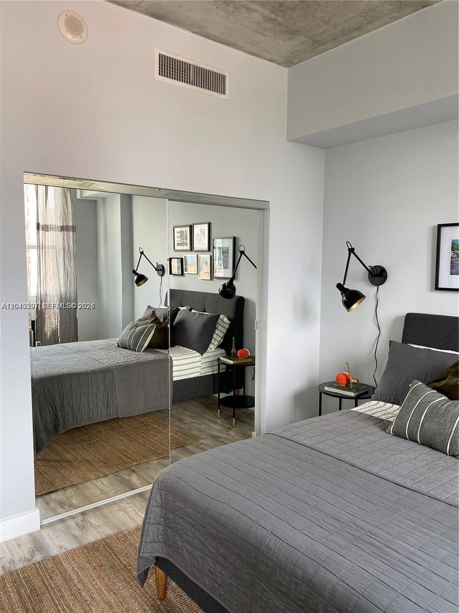 A bedroom features a gray bed, mirrored closet doors, and black wall-mounted lamps — 133 NE 2nd Ave # 915, Miami FL 33132, MIAMI, FL