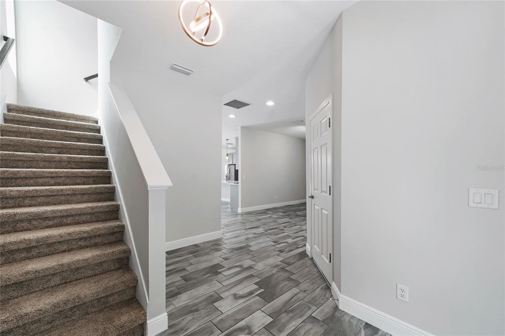 A carpeted staircase leads upward next to a hallway with gray wood-look tile flooring — 13000 BURNS DRIVE, ODESSA, FL