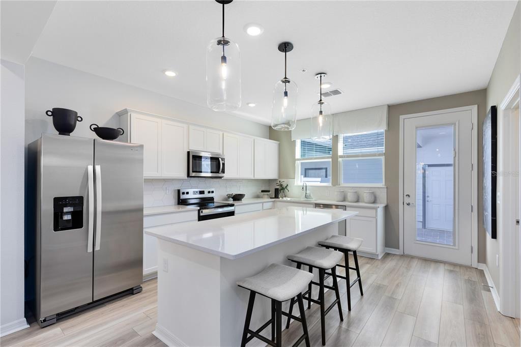 A modern kitchen features white cabinetry, stainless steel appliances, a quartz island, and three barstools — 4580 ORCHARD VIEW ALLEY, CLERMONT, FL