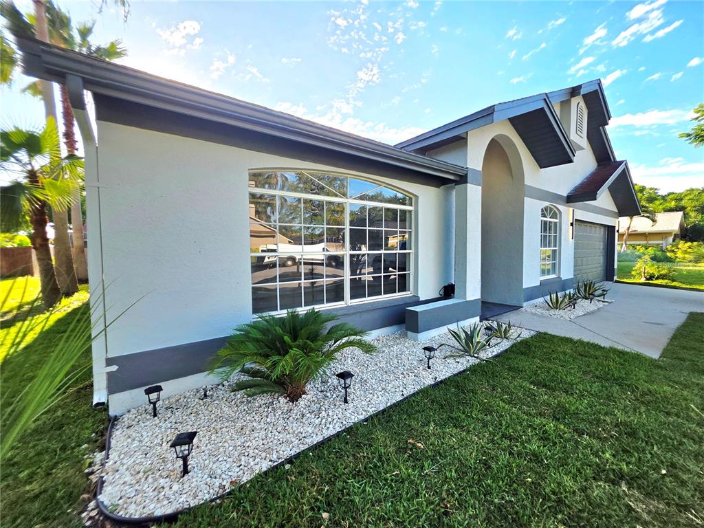 A single-story house exterior features a white facade, gray trim, a large window, and landscaping — 2796 CHALLENGER DRIVE, PALM HARBOR, FL