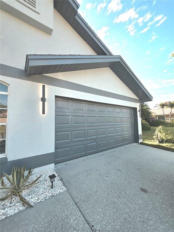A gray garage door is set into a white stucco wall with gray trim — 2796 CHALLENGER DRIVE, PALM HARBOR, FL