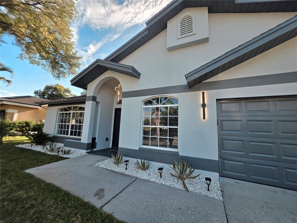 A single-story house exterior features white stucco walls, gray trim, a garage, and landscaping — 2796 CHALLENGER DRIVE, PALM HARBOR, FL