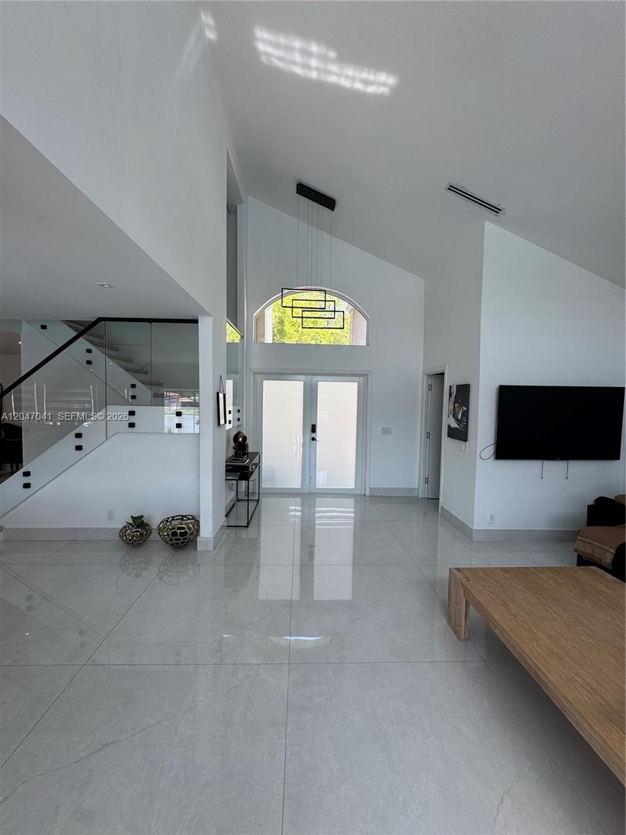 A bright, high-ceilinged foyer features white tile floors, a glass-railed staircase, and a double-door entrance — 4943 SW 33rd Way, Hollywood FL 33312, HOLLYWOOD, FL