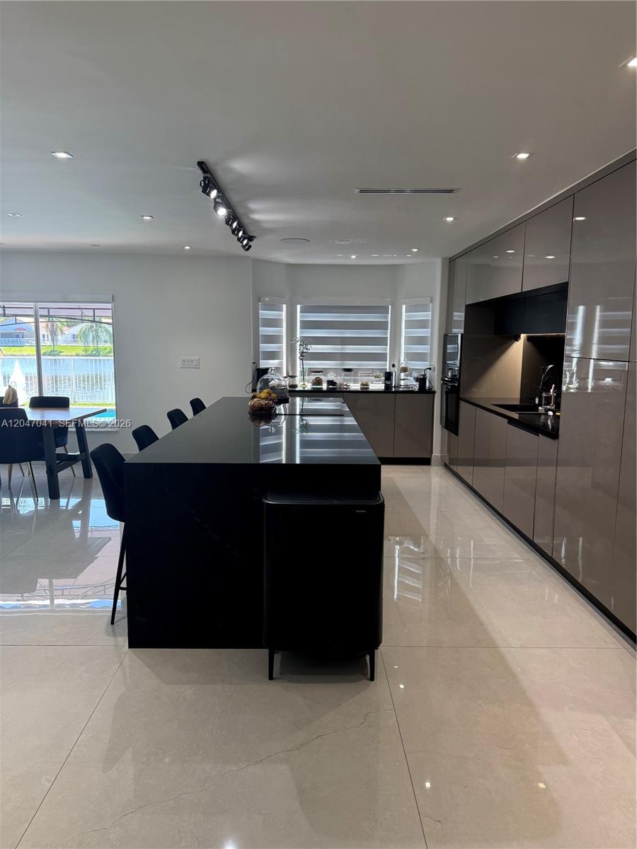 A modern kitchen features a large black island, glossy taupe cabinetry, and large floor tiles — 4943 SW 33rd Way, Hollywood FL 33312, HOLLYWOOD, FL