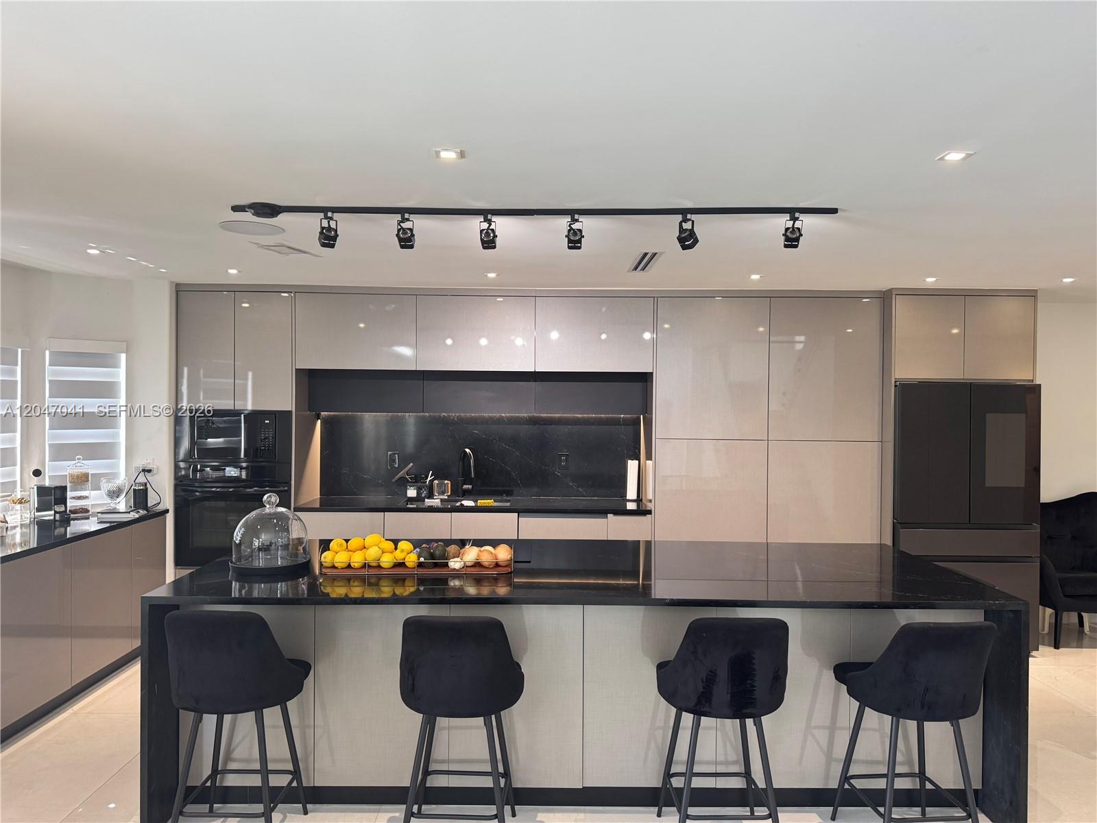A modern kitchen features a black island, glossy cabinets, and track lighting — 4943 SW 33rd Way, Hollywood FL 33312, HOLLYWOOD, FL