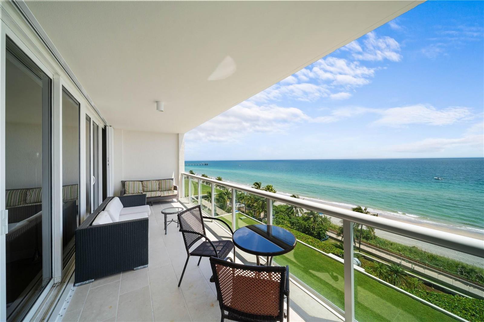 A balcony with outdoor furniture overlooks a beach, ocean, and green lawn — 6001 N Ocean Drive # 706, Hollywood FL 33019, HOLLYWOOD, FL