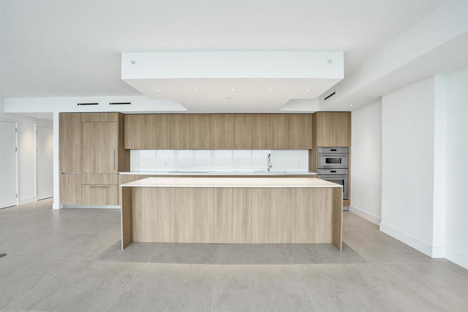 A modern kitchen features light wood cabinetry, a white island, and gray tile flooring — 407 N Riverside Drive # 602, Pompano Beach FL 33062, POMPANO BEACH, FL