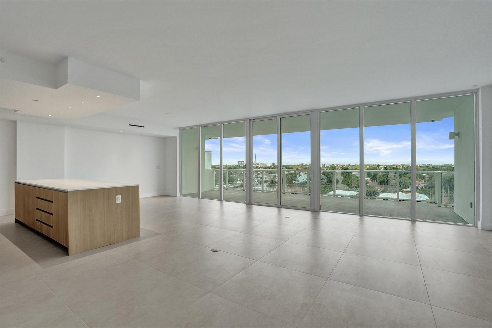 An open-plan living area features large glass sliding doors, light tile flooring, and a kitchen island — 407 N Riverside Drive # 602, Pompano Beach FL 33062, POMPANO BEACH, FL