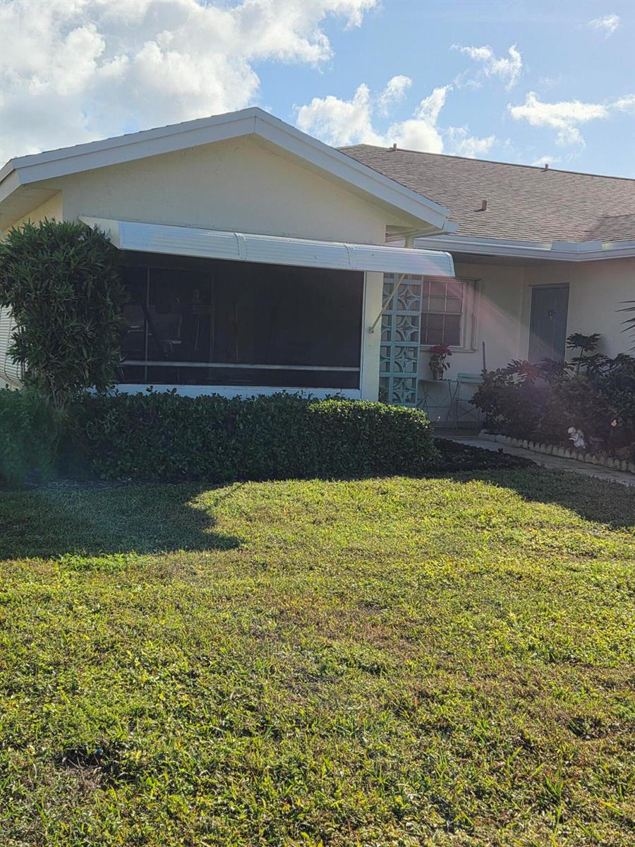 A low-angle exterior view of a house with a screened-in porch and a front lawn — 5042 Lakefront Boulevard # A, Delray Beach FL 33484, DELRAY BEACH, FL