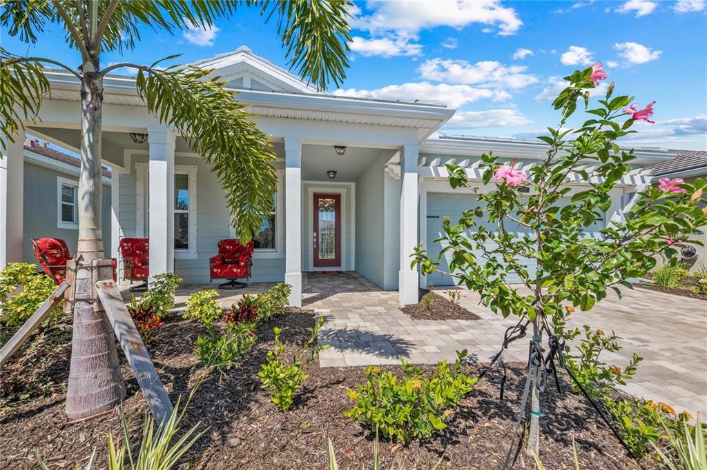 A single-story house with a covered porch, red front door, and a paved driveway — 5697 LONG SHORE LOOP, SARASOTA, FL