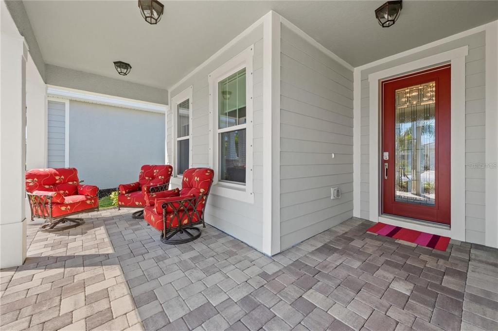 A covered front porch features gray siding, a red front door, and three red chairs — 5697 LONG SHORE LOOP, SARASOTA, FL