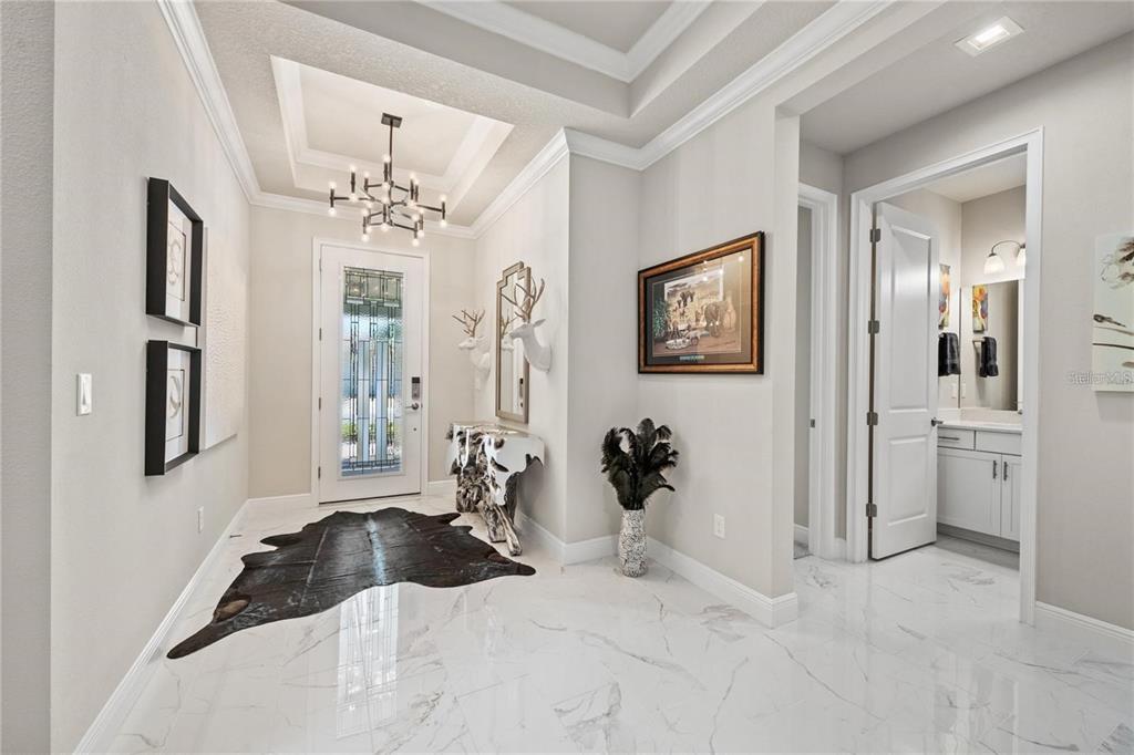 A bright foyer features white marble floors, a tray ceiling, and a modern chandelier — 5697 LONG SHORE LOOP, SARASOTA, FL